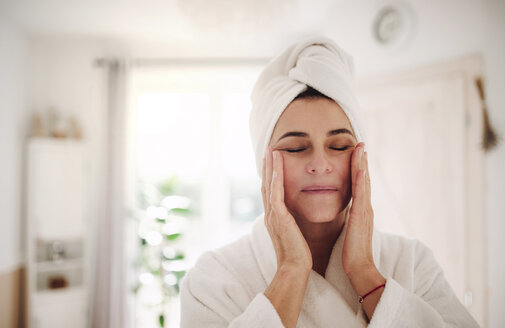 Portrait of mature woman in a bathroom at home applying moisturizer - HAPF02952