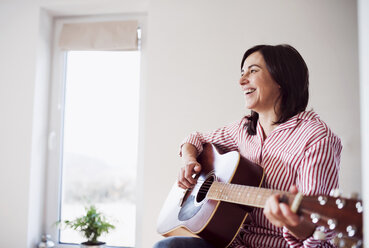 Glückliche reife Frau spielt Gitarre zu Hause - HAPF02957