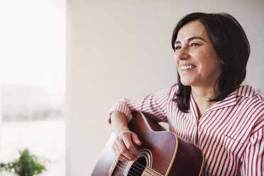 Portrait of smiling mature woman playing guitar at home - HAPF02958