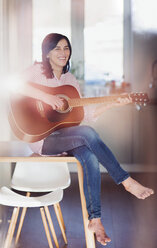 Smiling mature woman playing guitar at home - HAPF02960