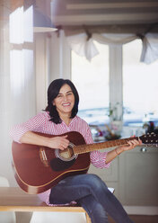 Portrait of smiling mature woman playing guitar at home - HAPF02961