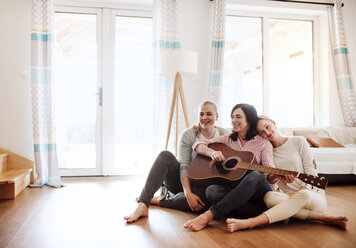Reife Frau mit zwei Töchtern sitzt auf dem Boden und spielt Gitarre zu Hause - HAPF02962