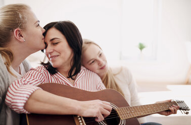 Reife Frau mit zwei liebevollen Töchtern, die zu Hause Gitarre spielen - HAPF02964