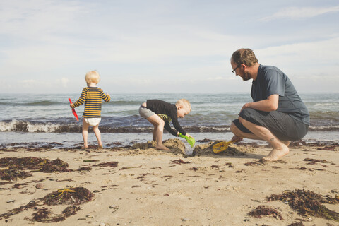 Vater mit zwei Kindern beim Spielen am Strand, lizenzfreies Stockfoto