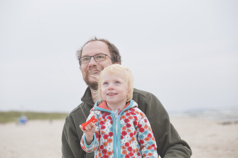 Vater und kleine Tochter spielen mit Drachen am Strand, lizenzfreies Stockfoto