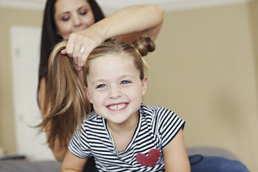 Mother styling hair of daughter on bed - BLEF05610