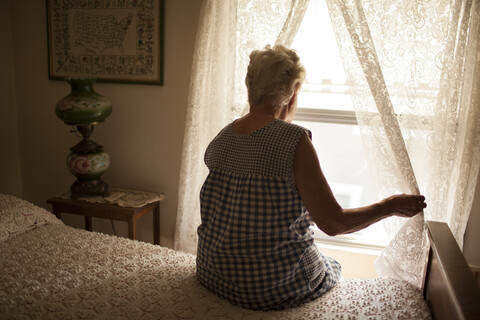 Nachdenkliche ältere Frau schaut aus dem Schlafzimmerfenster, lizenzfreies Stockfoto