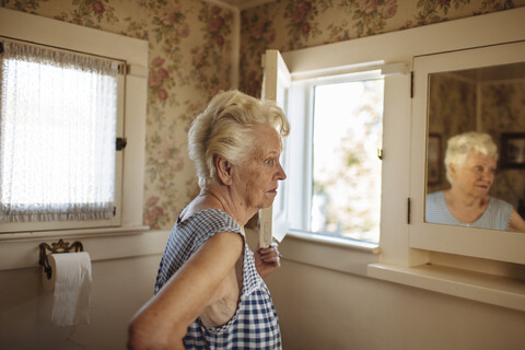 Ältere kaukasische Frau, die sich im Spiegel betrachtet, lizenzfreies Stockfoto