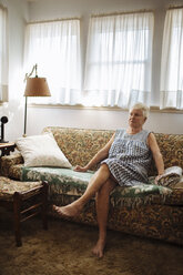 Ältere Frau sitzt auf dem Sofa im Wohnzimmer - BLEF05661