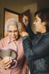 Enkelin kämmt die Haare der Großmutter, die einen Spiegel hält - BLEF05673