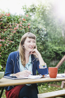 Mixed race businesswoman writing notes in backyard - BLEF05687