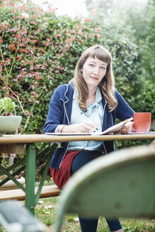 Mixed race businesswoman writing notes in backyard - BLEF05688