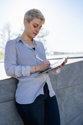 Junge Frau lehnt an der Wand und benutzt ein digitales Tablet - FBAF00602