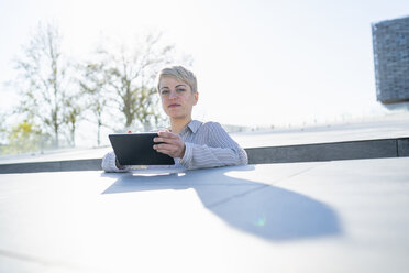 Porträt einer jungen Frau, die sich mit einem digitalen Tablet an die Wand lehnt - FBAF00605