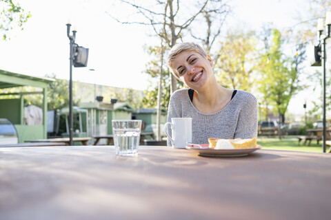 Porträt einer lächelnden Frau mit einer Tasse Kaffee und einem Stück Kuchen im Freien, lizenzfreies Stockfoto