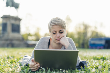 Porträt einer nachdenklichen jungen Frau, die auf einer Wiese liegt und ein digitales Tablet benutzt - FBAF00616