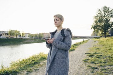 Young woman with cell phone outdoors looking at distance - FBAF00619