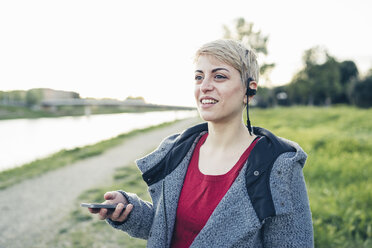 Portrait of smiling woman using smartphone and headset outdoors - FBAF00620