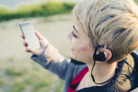 Lächelnde Frau mit Smartphone und Headset im Freien, Nahaufnahme, lizenzfreies Stockfoto