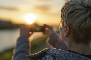 Rückenansicht einer Frau, die den Sonnenuntergang fotografiert, Nahaufnahme - FBAF00629