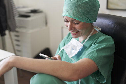 Happy woman in scrubs having a break using cell phone - PNEF01484