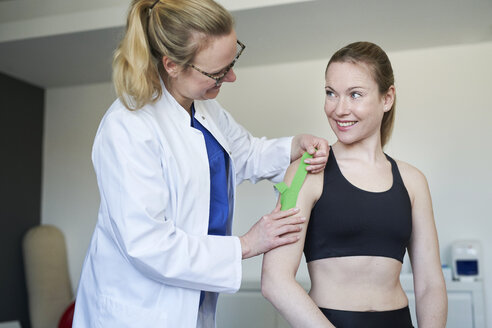 Ärztin beim Anlegen eines Pflasters an der Schulter eines Patienten in einer Arztpraxis - PNEF01514