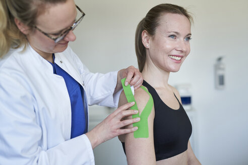 Ärztin beim Anlegen eines Pflasters an der Schulter eines Patienten in einer Arztpraxis - PNEF01515