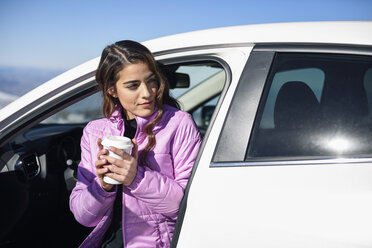 Frau sitzt im Auto und trinkt einen heißen Kaffee vor dem Skifahren - JSMF01093