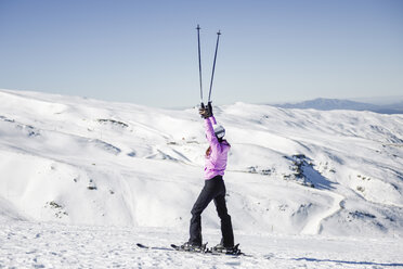 Glückliche Frau, die ihre Skistöcke in einer schneebedeckten Landschaft in der Sierra Nevada, Andalusien, Spanien, hochhält - JSMF01100