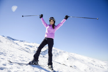 Glückliche Frau, die ihre Skistöcke in einer schneebedeckten Landschaft in der Sierra Nevada, Andalusien, Spanien, hochhält - JSMF01105