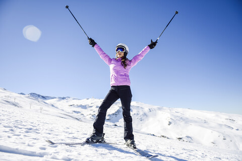 Glückliche Frau, die ihre Skistöcke in einer schneebedeckten Landschaft in der Sierra Nevada, Andalusien, Spanien, hochhält, lizenzfreies Stockfoto