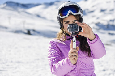 Woman in ski clothes filming with an action camera in snow covered-landscape - JSMF01111