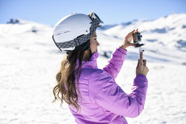 Woman in ski clothes filming with an action camera in snow covered-landscape - JSMF01116