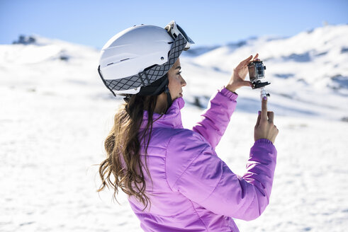 Frau in Skikleidung filmt mit einer Action-Kamera in einer verschneiten Landschaft - JSMF01116