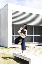 Female ballet dancer using tablet in front of an office during work, standing on one leg - ERRF01415