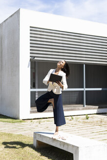 Balletttänzerin mit Tablet vor einem Büro während der Arbeit, auf einem Bein stehend - ERRF01416