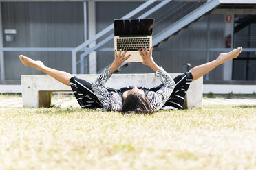 Female ballet dancer doing a spagat in front of an office, using laptop lying - ERRF01423