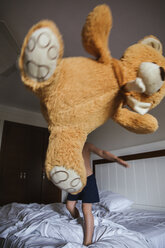Kleiner Junge steht auf dem Bett und wirft einen übergroßen Teddybär in die Luft - LJF00029