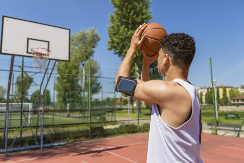 Junger Mann spielt Basketball, Smartphone in der Armtasche - MGIF00515