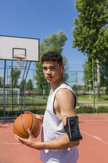 Junger Mann spielt Basketball, Smartphone in der Armtasche - MGIF00516