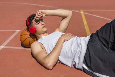 Young man lying on basketball, red headphones - MGIF00517
