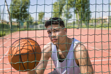 Junger Mann hält Basketball auf einem Gitter - MGIF00523