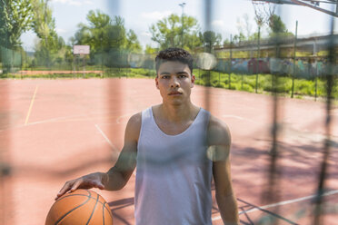 Junger Mann spielt Basketball und schaut in die Kamera, hinter dem Netz - MGIF00526