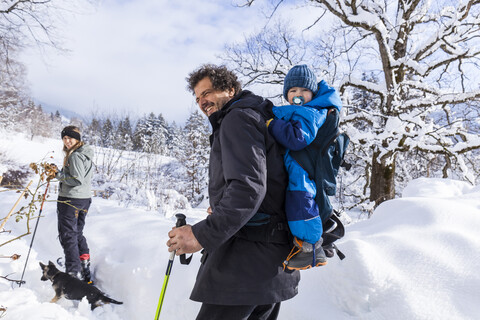 Vater mit Sohn in der Kindertrage, Mutter und Hund in Oberammergau im Winter, lizenzfreies Stockfoto