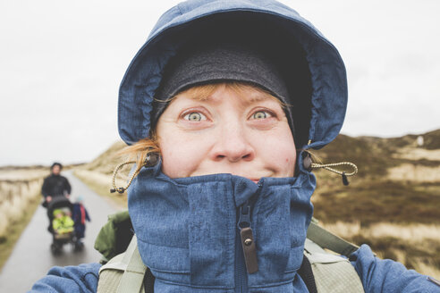 Mother taking selfie with her husband and kids in the background at stormy weather, Sylt, Germany - IHF00061