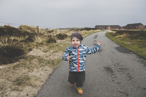 Porträt eines kleinen Jungen, der auf einer leeren Straße läuft, Sylt, Deutschland, lizenzfreies Stockfoto