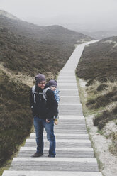 Mann trägt seinen kleinen Sohn in einer Babytrage auf dem Rücken, Sylt, Deutschland - IHF00064