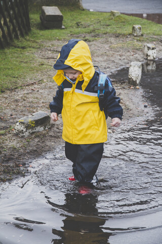 Kleiner Junge im Regenanzug erkundet eine Pfütze, Sylt, Deutschland, lizenzfreies Stockfoto