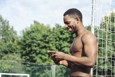 Sportler mit Smartphone auf dem Fußballplatz - AHSF00406