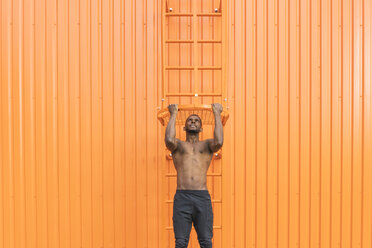 Athlete doing chin-ups in front of an orange wall - AHSF00409